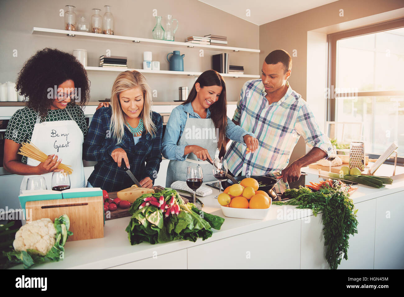 Group of four diverse friends preparing a meal with vegetables and fruit in kitchen for themselves or a culinary class Stock Photo
