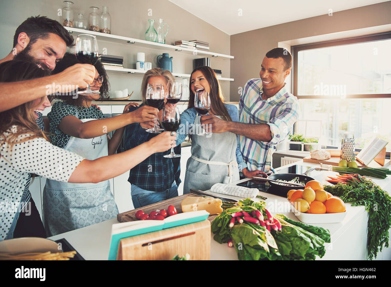 Mixed group of young adult celebrating friends having a cooking party in front of kitchen table with vegetables and fruit on top Stock Photo