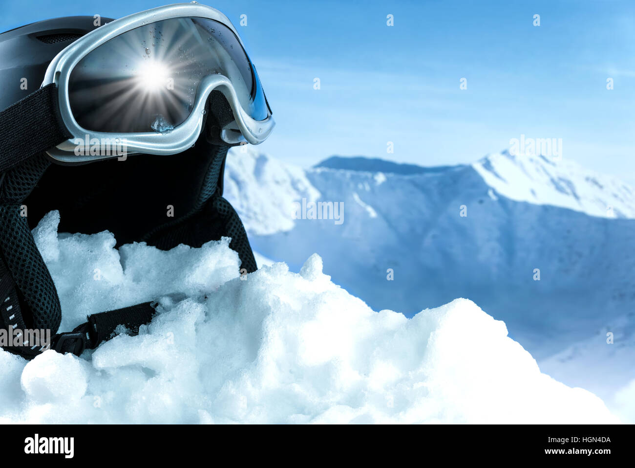Helmet and ski goggles on snow with a blue sky and mountains Stock