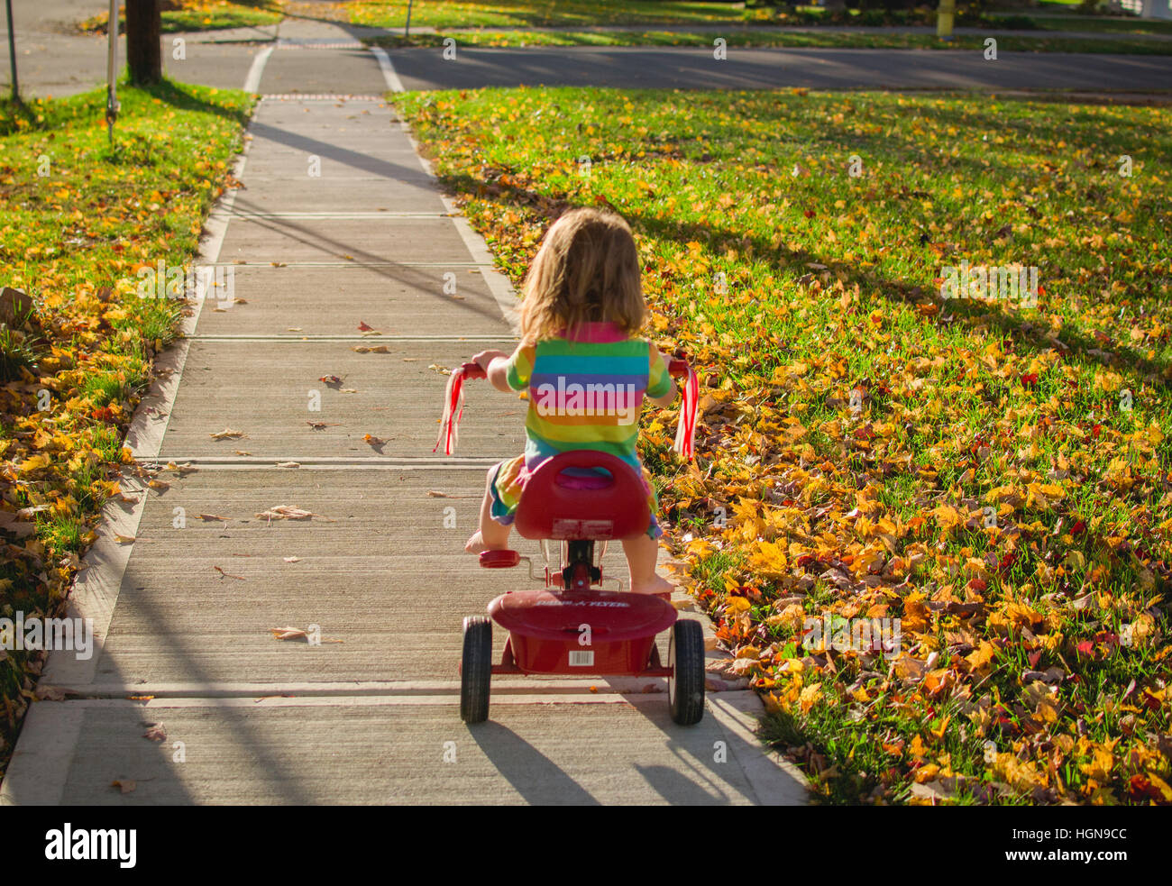 A young girl rides a tricycle in a small town in the United States. Stock Photo