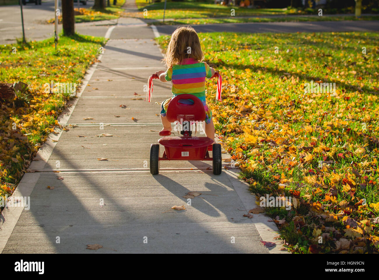 A young girl rides a tricycle in a small town in the United States. Stock Photo