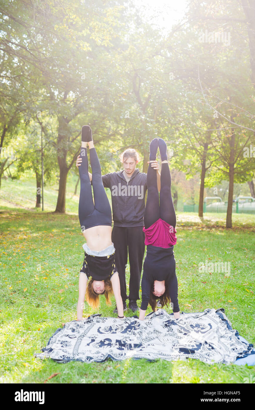 Handstand Outside Man teaching two young girls how to handstand outdoor in a park in ...