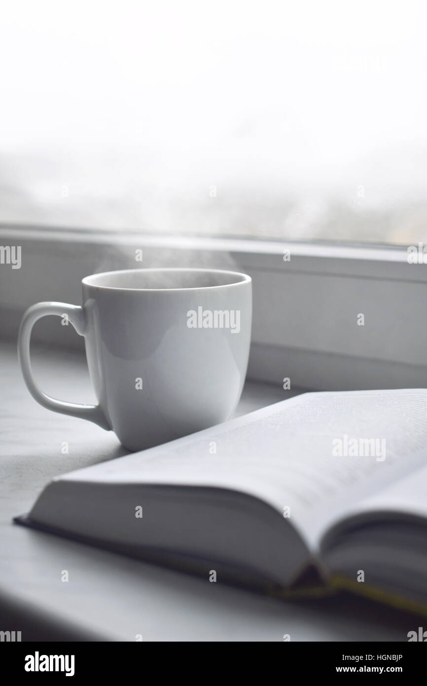 Cozy winter still life: cup of hot coffee and opened book on vintage  windowsill against snow landscape from outside Stock Photo - Alamy