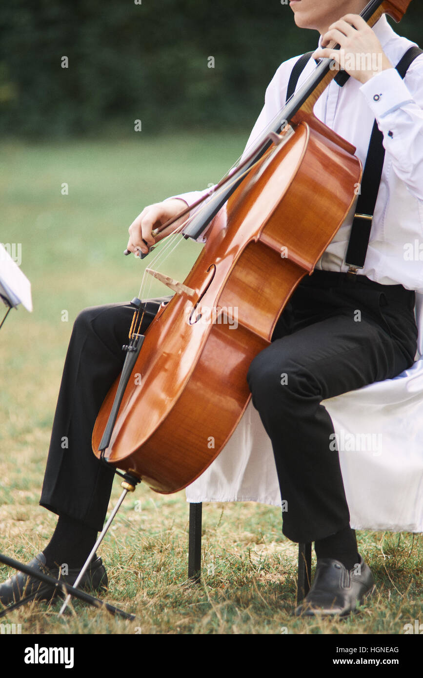 Young man playing cello outside. Cellist playing classical music on