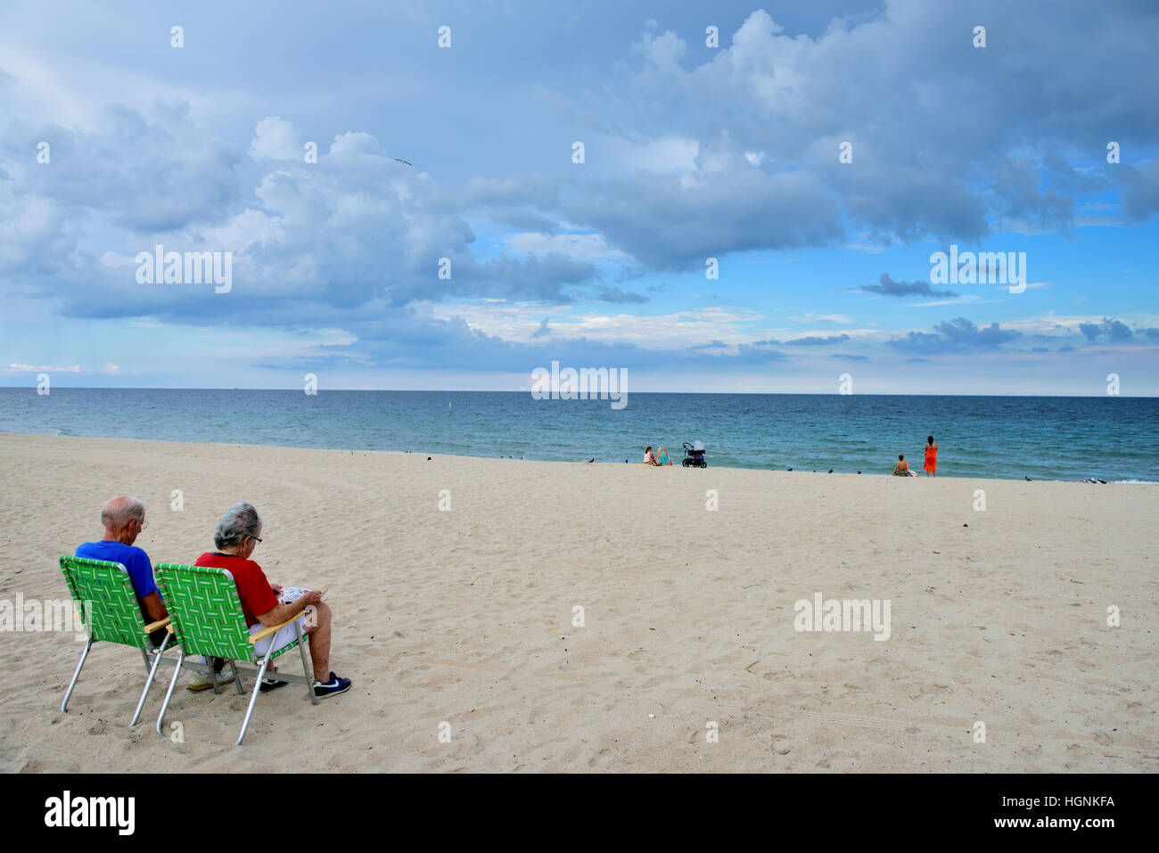 Older couple sitting on lounge chairs by sea and sandy beach Stock Photo
