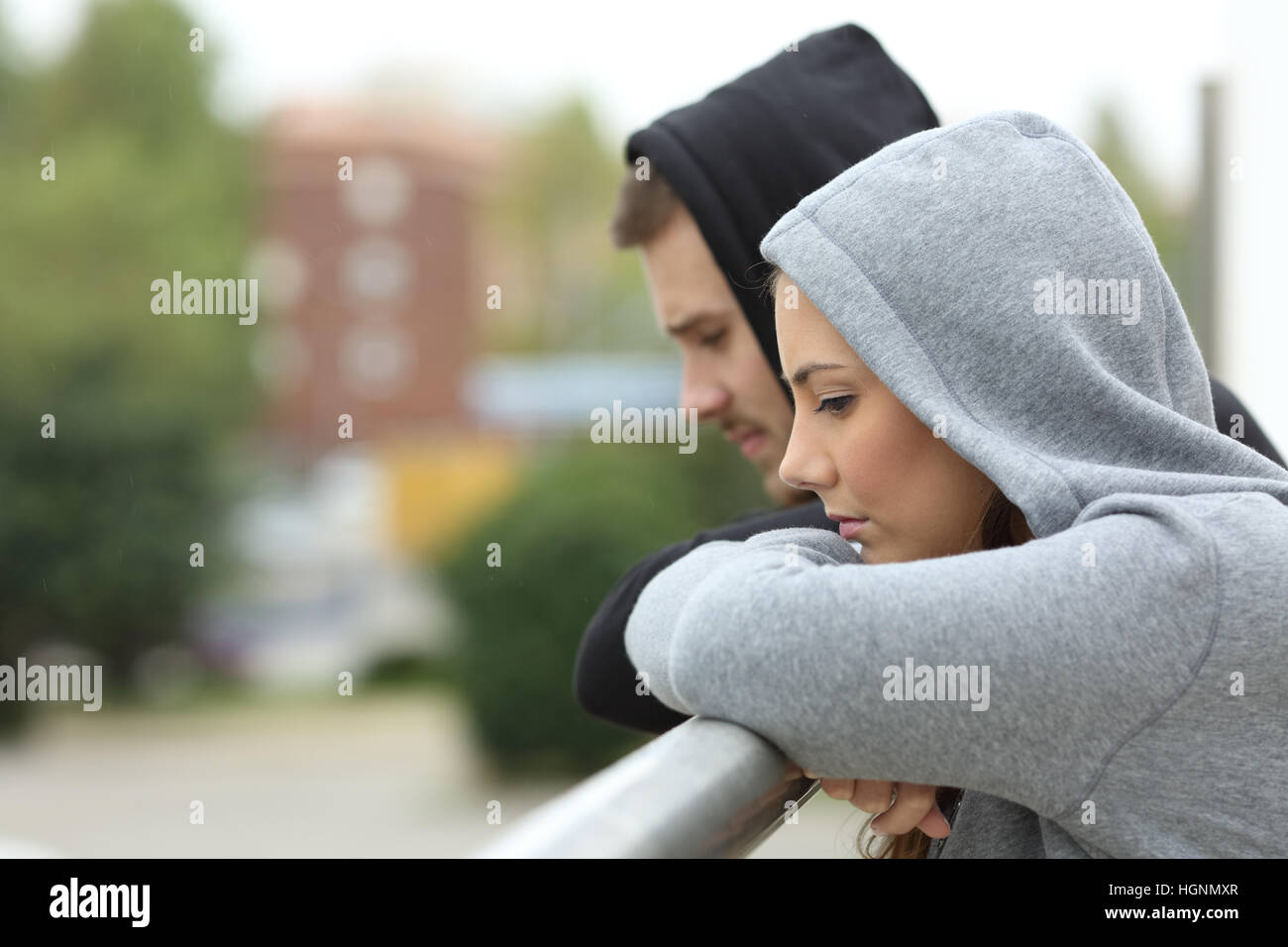 Side view of a sad couple of teens looking down after break up in a balcony of a house with an urban background Stock Photo