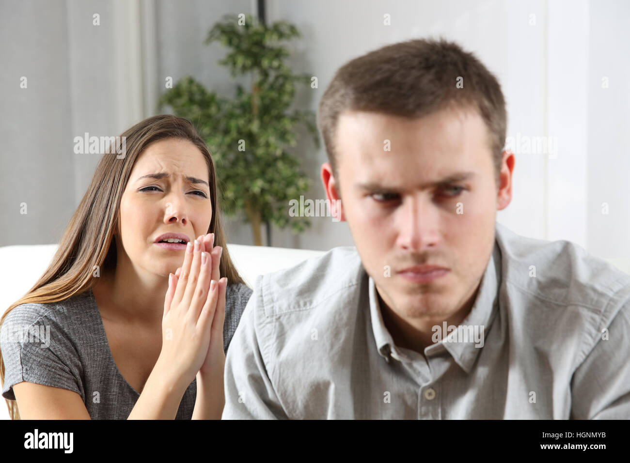 Wife asking for forgiveness to her ex husband after conflict sitting on a couch in the living room of a house Stock Photo