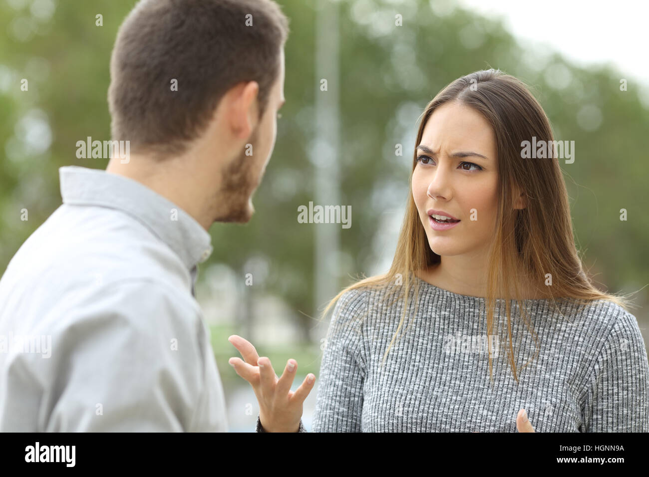 Couple talking seriously outdoors in a park with a green background Stock Photo