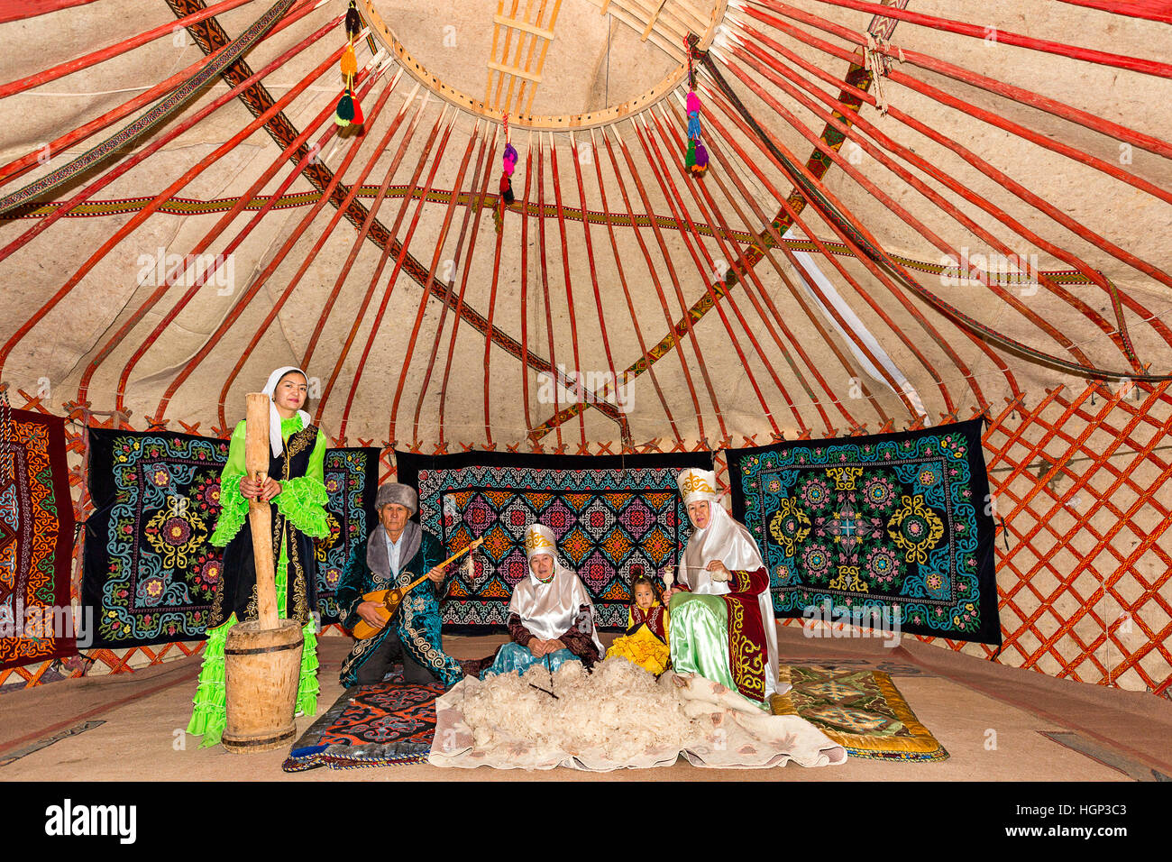 Kazakh people in a nomadic yurt with a woman who spins the wool and a man playing local musical instrument of dombra in Almaty, Stock Photo