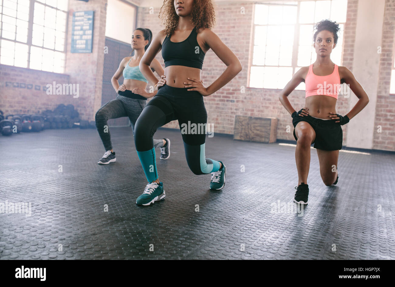 Portrait of three young women doing workout together in gym. Females exercising in fitness class. Stock Photo