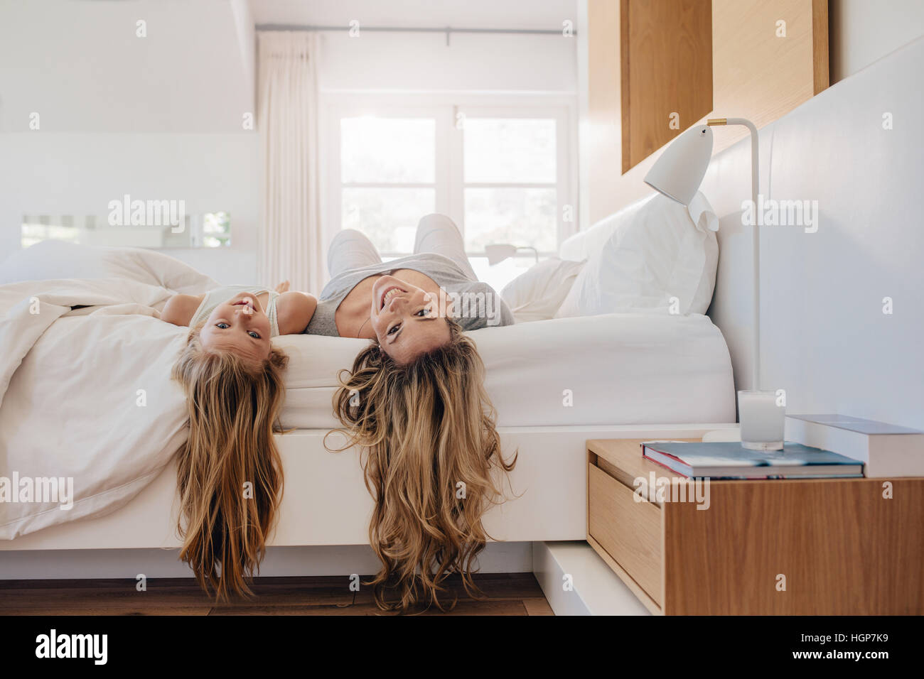 Young woman and a girl lying on bed. Mother and daughter in bedroom. Stock Photo