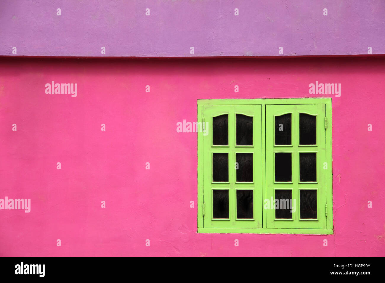 Close up of a brightly colored building with pink walls, lime green windows & purple roof, Caribbean. Stock Photo