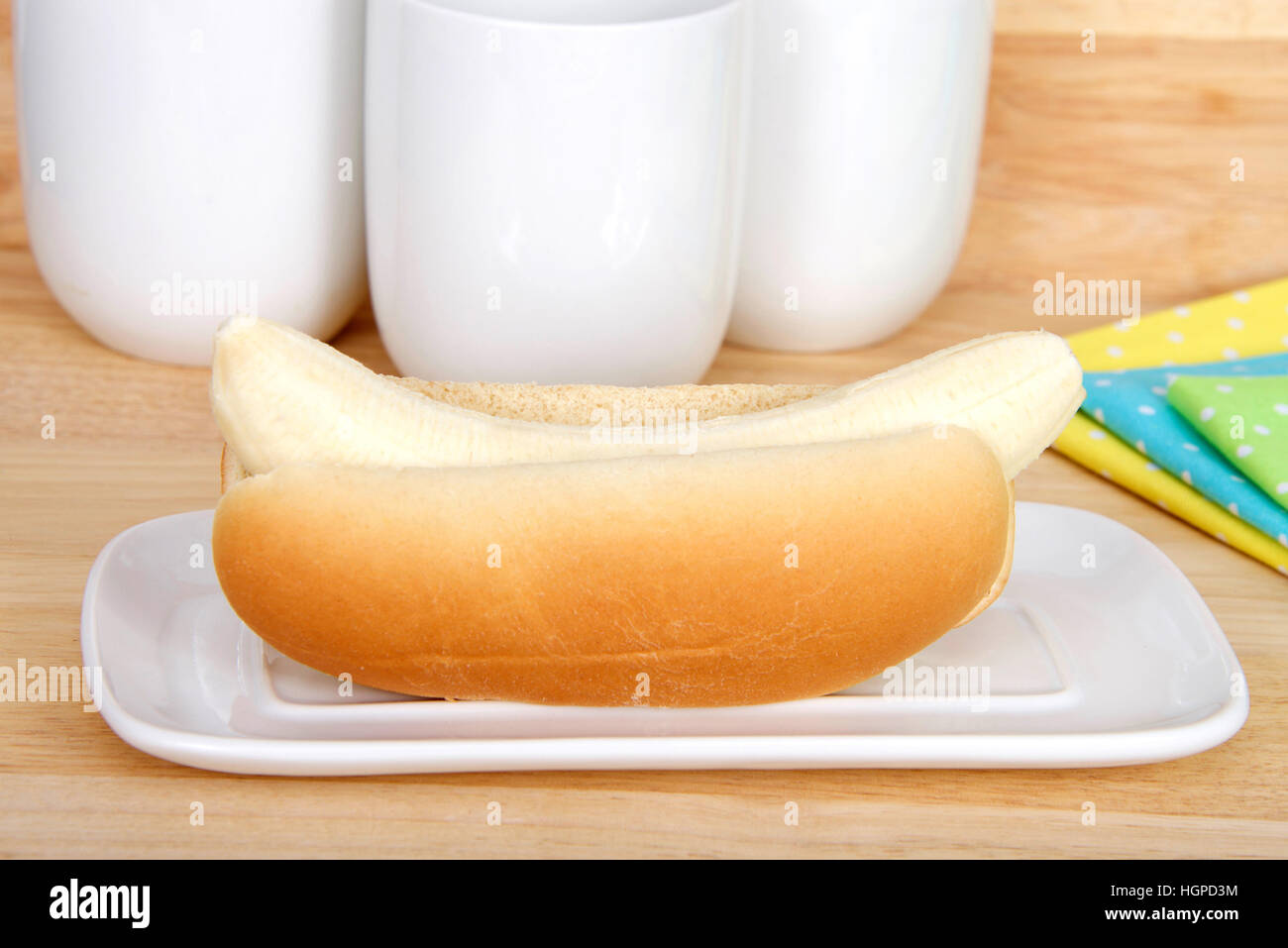 Banana in a hot dog bun served on a white rectangular plate, yellow