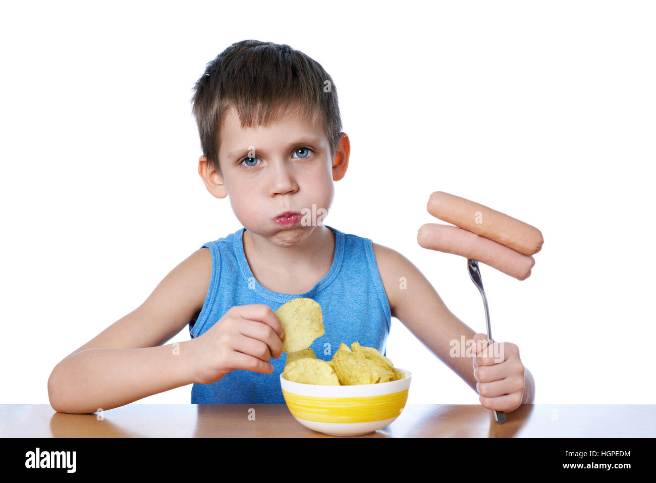Little boy with fat cheeks eating sausages and potato chips isolated white Stock Photo