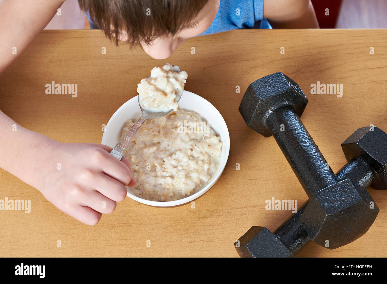 Boy eating porridge and dumbbells as symbols of sports lifestyle Stock Photo