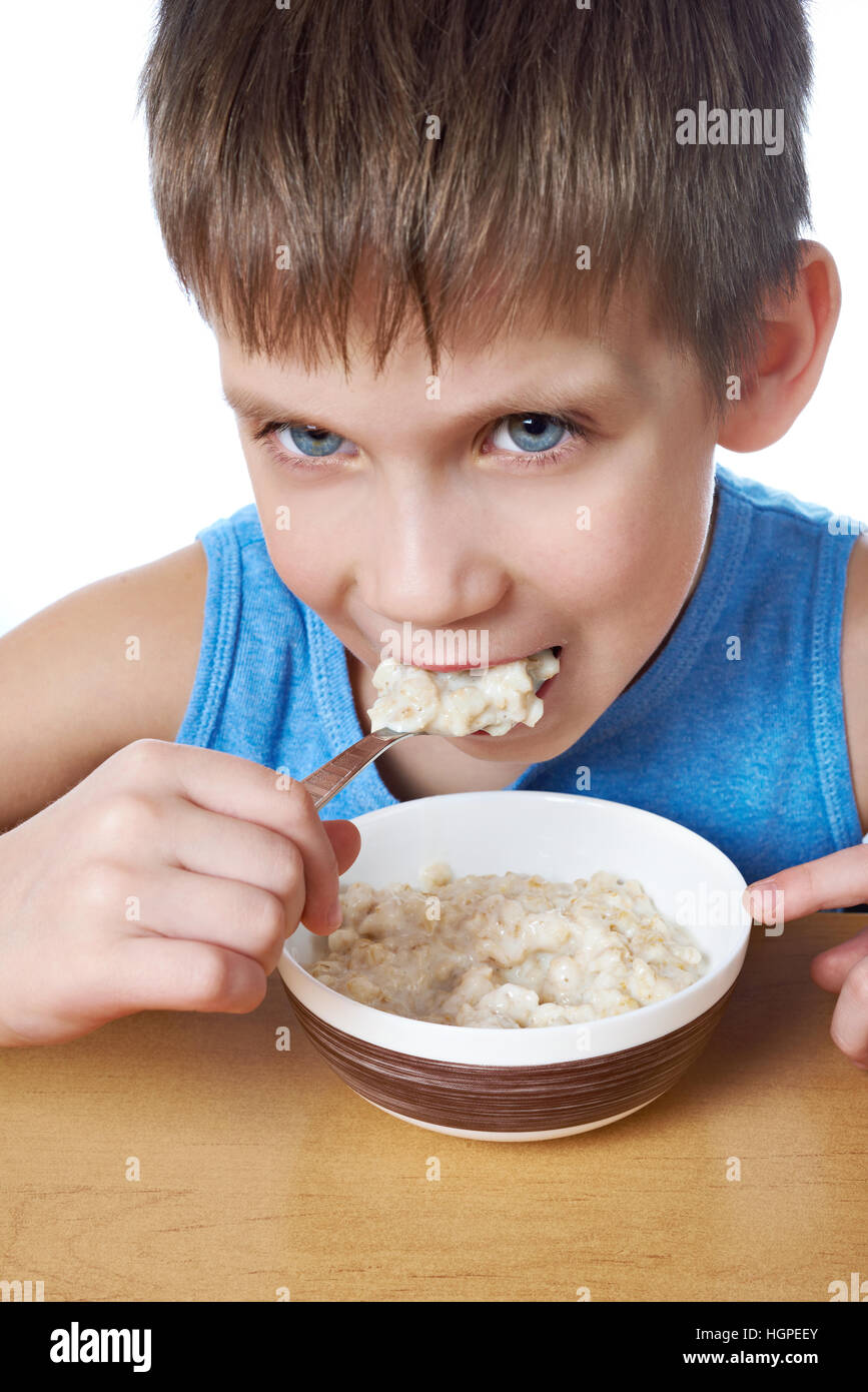 Little boy eating porridge at the table isolated white Stock Photo