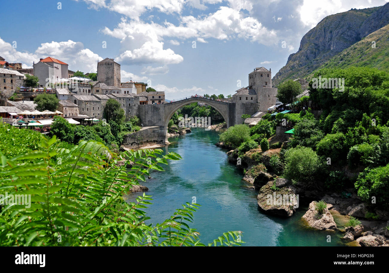 16th-century Ottoman Bridge over a river in a mountain village in Bosnia Herzegovina, with blue cloudy sky and sun shining Stock Photo