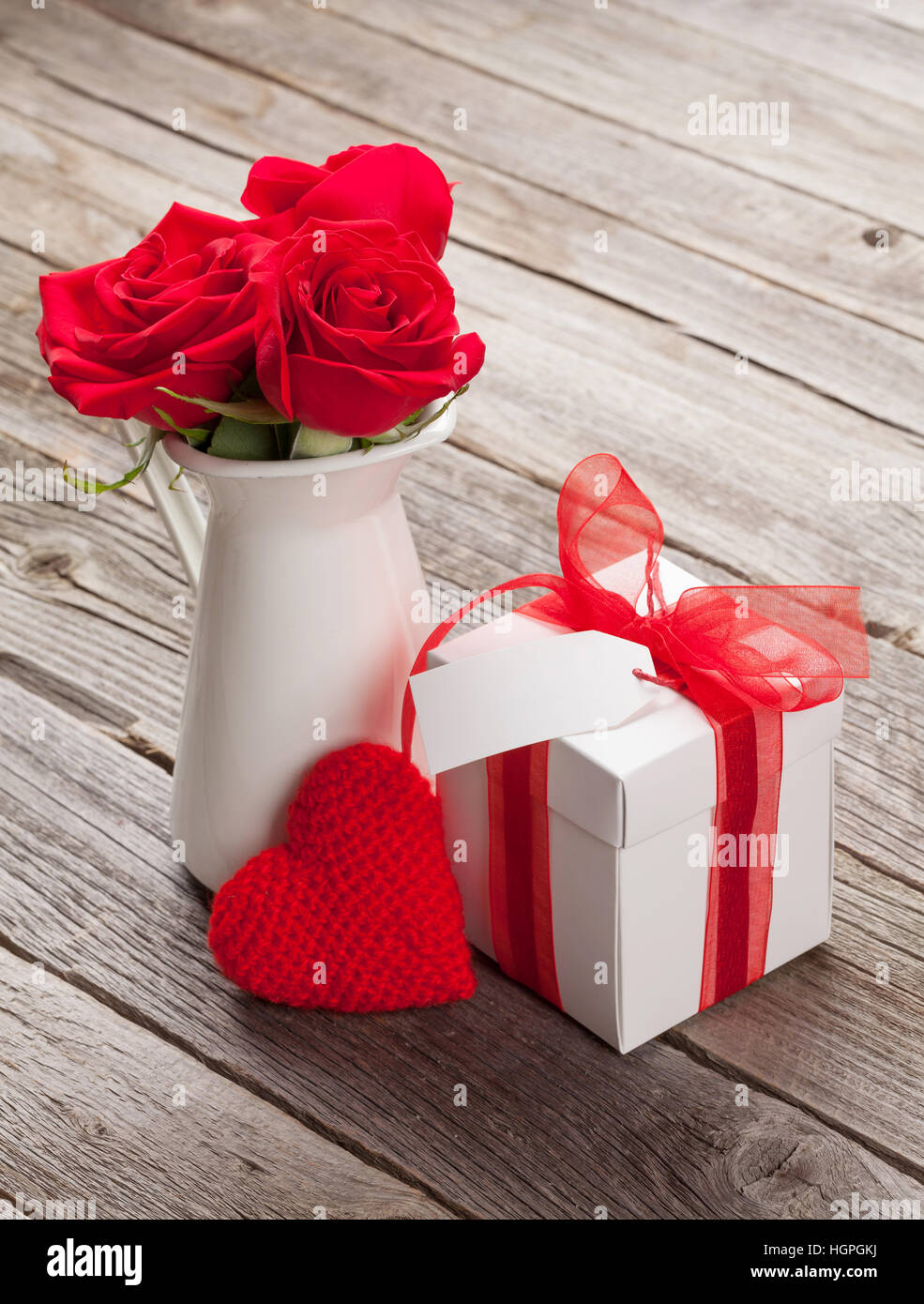 Red rose flowers in pitcher and Valentines day gift box on wooden table Stock Photo