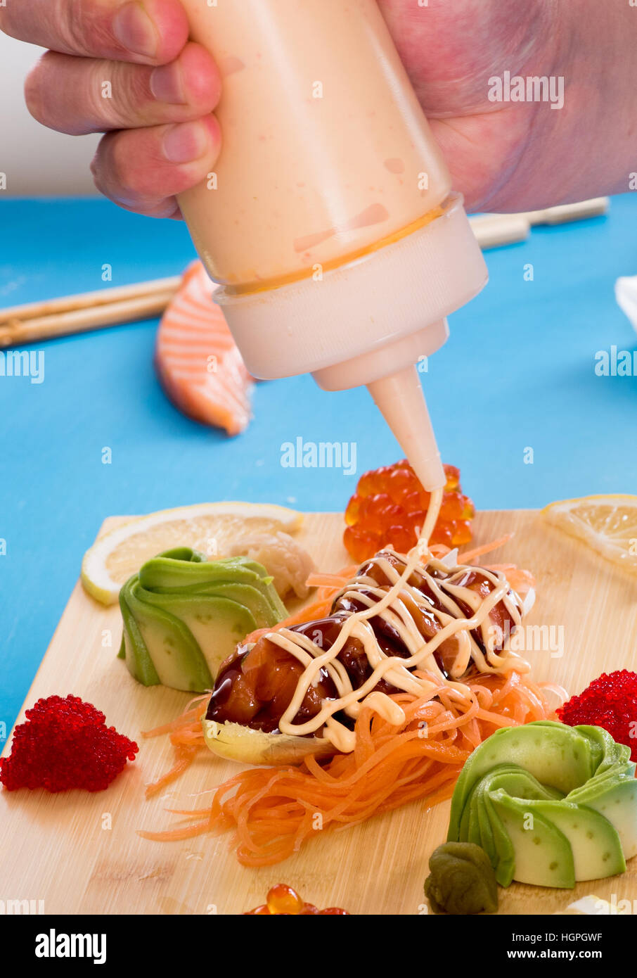 Chef adding sauce to a plate of salmon tartare served with avocado pear and red caviar or fish roe on a wooden board, close up of his hand Stock Photo
