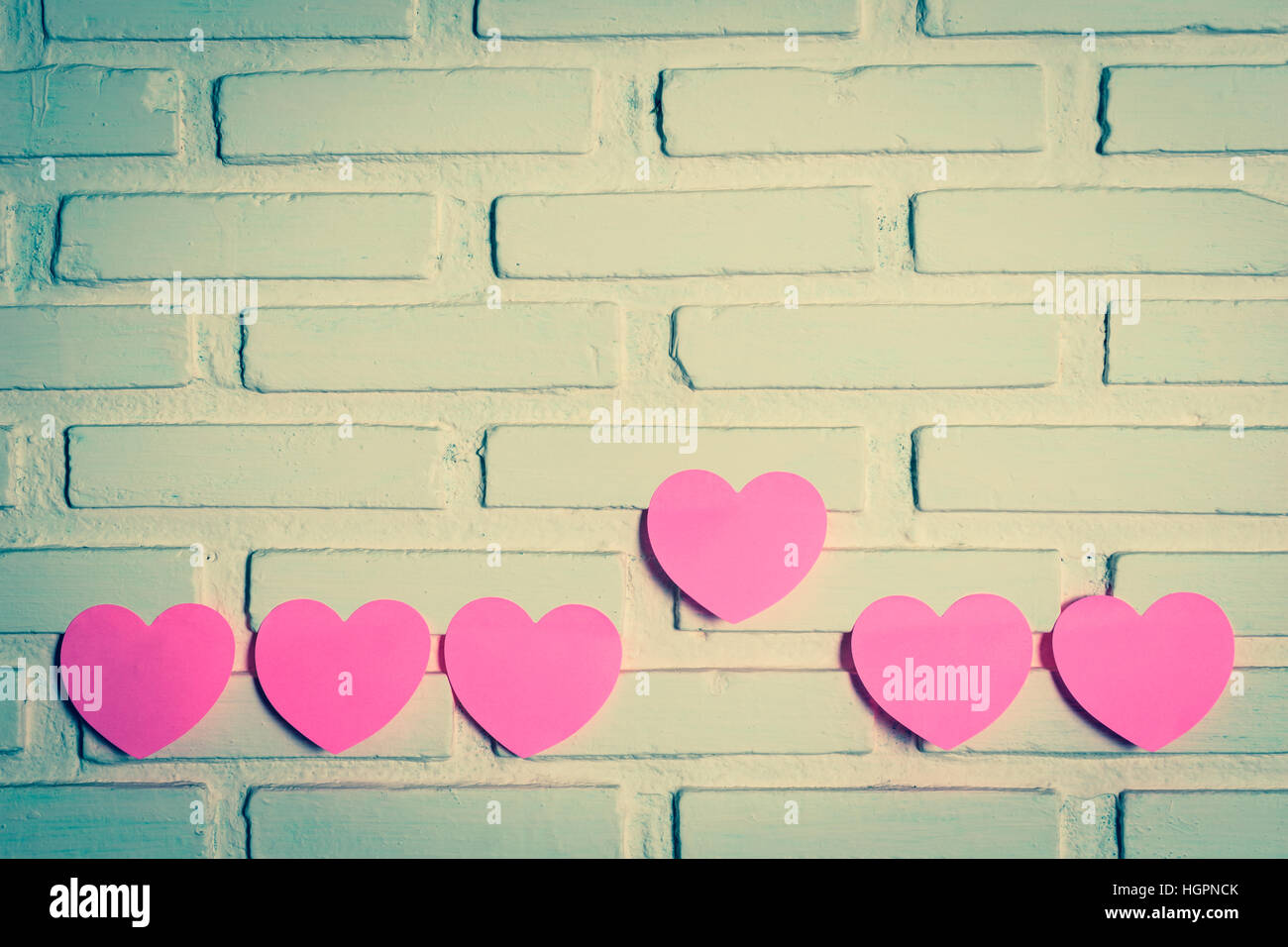 Pink sticky notes hearts shaped lined holes on the wall and a heart the outstanding one. vintage style Stock Photo