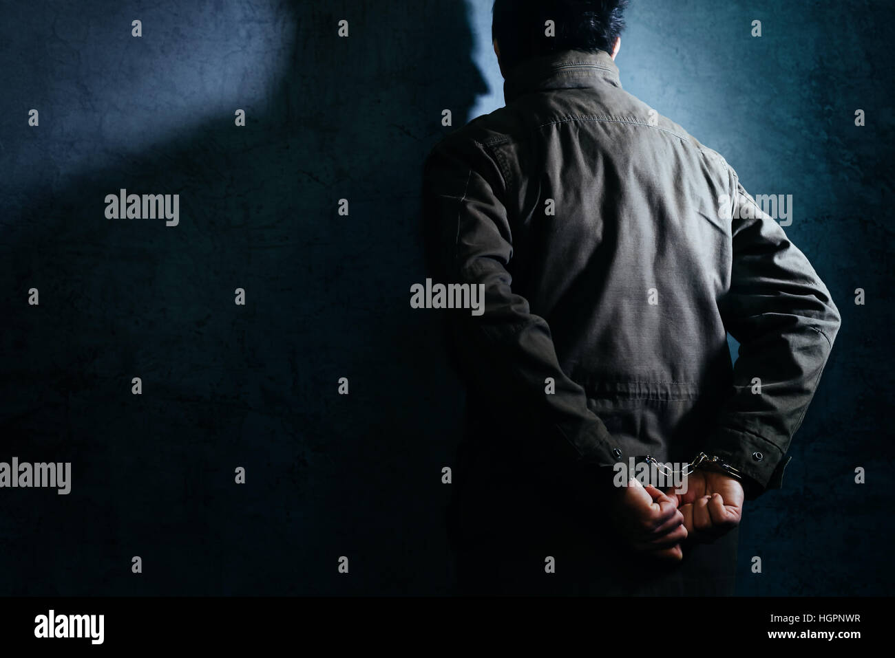 Arrested male criminal with handcuffs facing prison wall as copy space Stock Photo