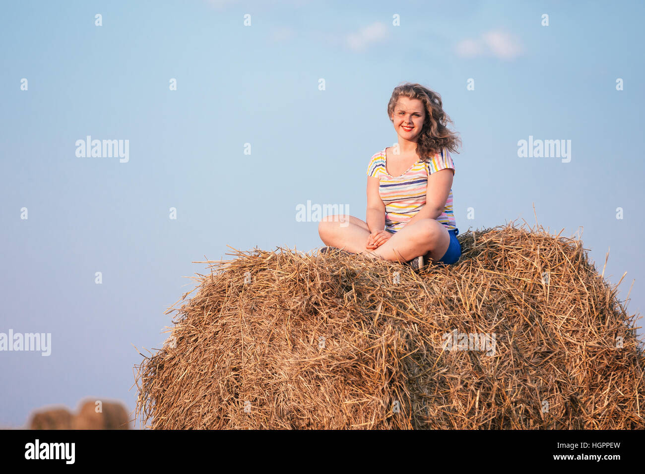 Beautiful Plus Size Young Woman In Shirt Sit On Hay Bales In Summer Field Meadow At Blue Sly Background Stock Photo