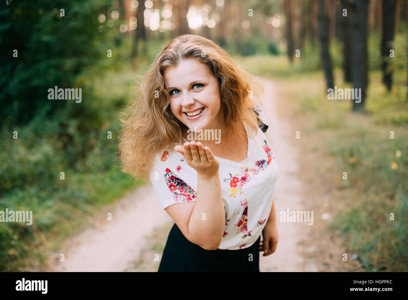 Portrait Of Young Pretty Plus Size Caucasian Happy Smiling Girl Woman With Blue Eyes, Wavy Brown Long Hair In White T-Shirt With Floral Print Sending Stock Photo