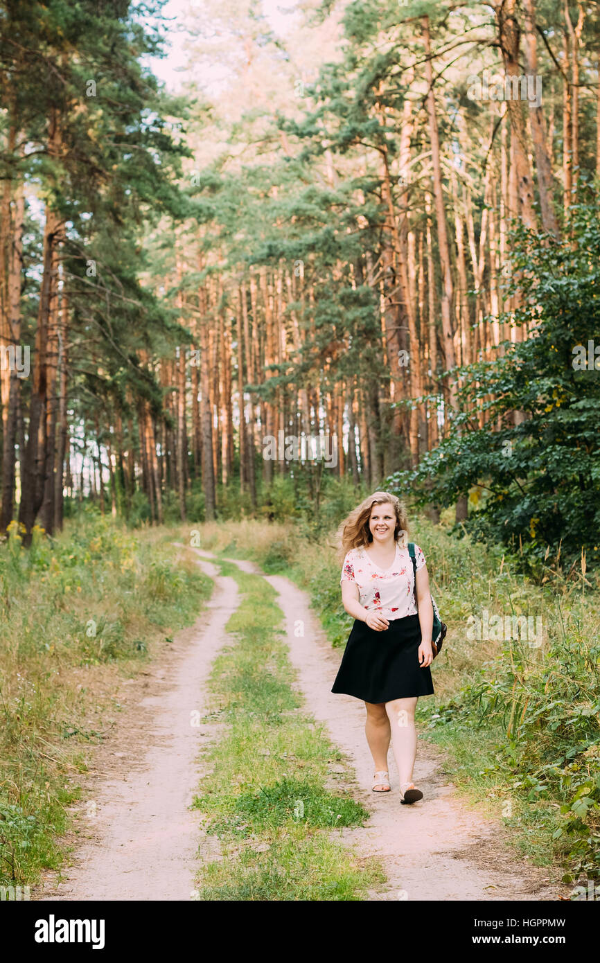 Young Pretty Plus Size Caucasian Happy Smiling Girl Woman In White T-Shirt And Black Short Skirt Walking Full-Length On Road In Summer Pine Forest Stock Photo
