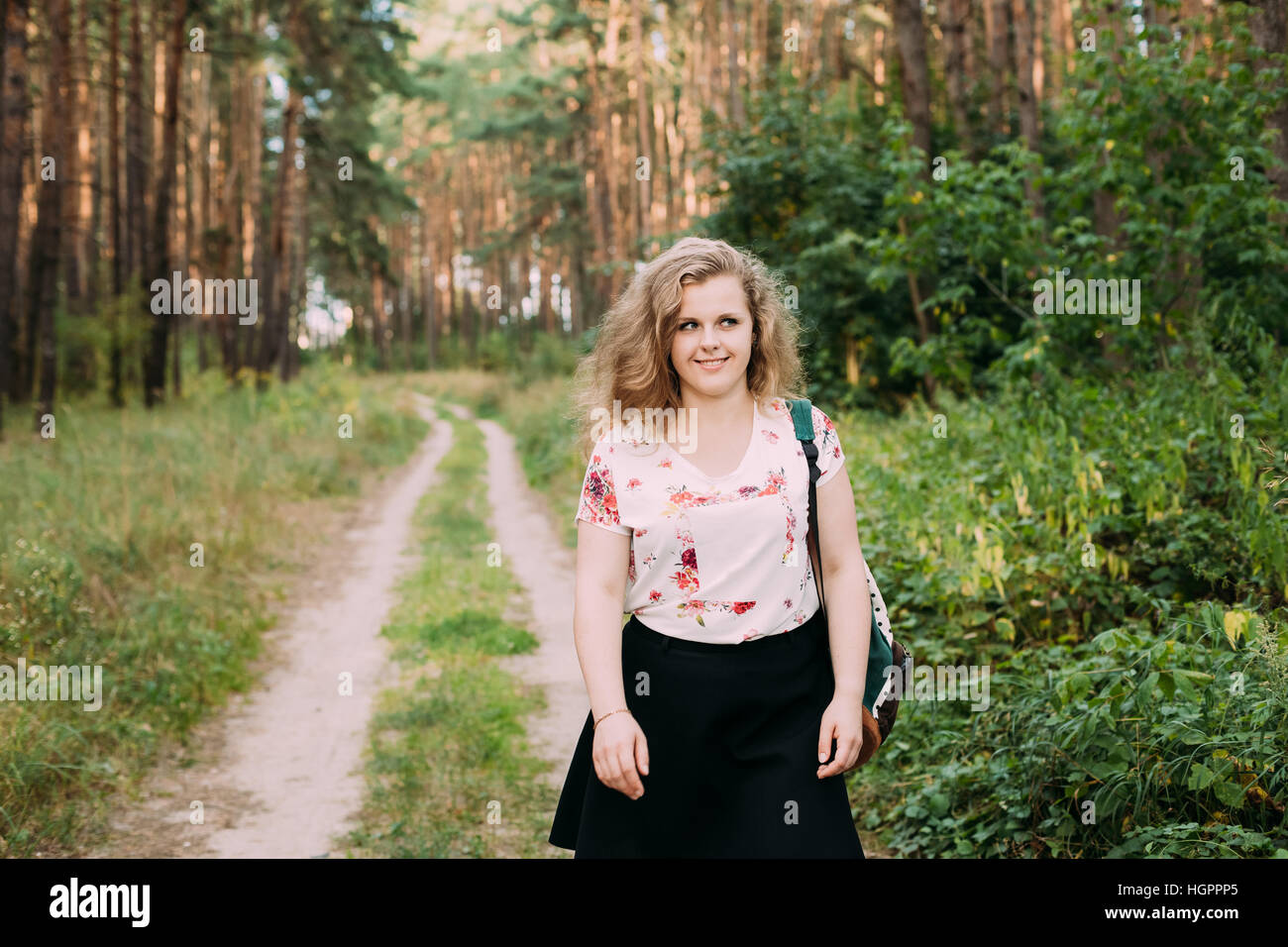 Young Pretty Plus Size Caucasian Happy Smiling Girl Woman In White T-Shirt And Black Short Skirt Walking Full-Length On Road In Summer Pine Forest Stock Photo