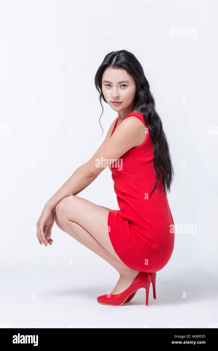 Side view of young woman in red dress and red shoes sitting Stock Photo ...