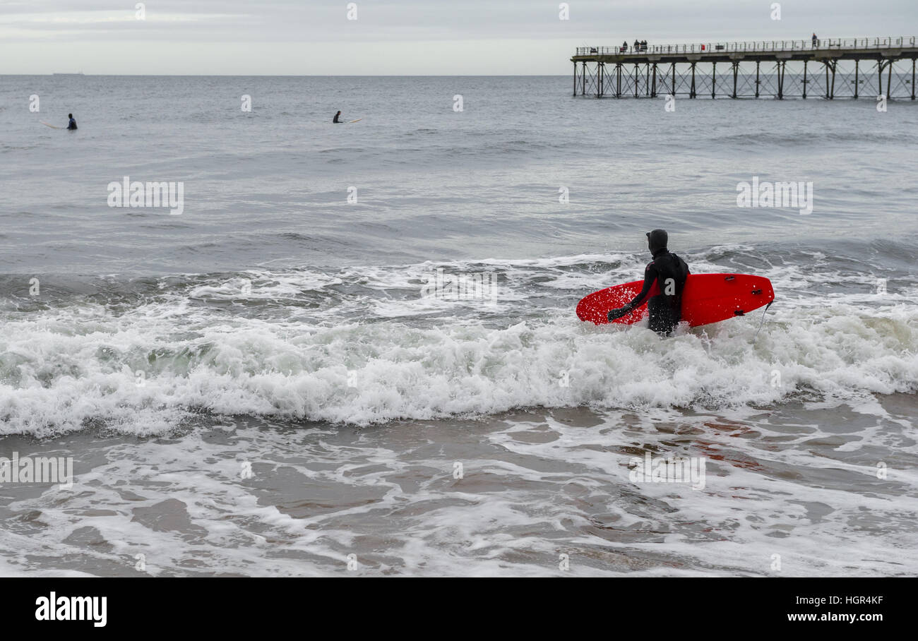 Man wearing a wet suit and carrying a surfboard in the sea at Saltburn, Yorkshire, England, U.K. Stock Photo