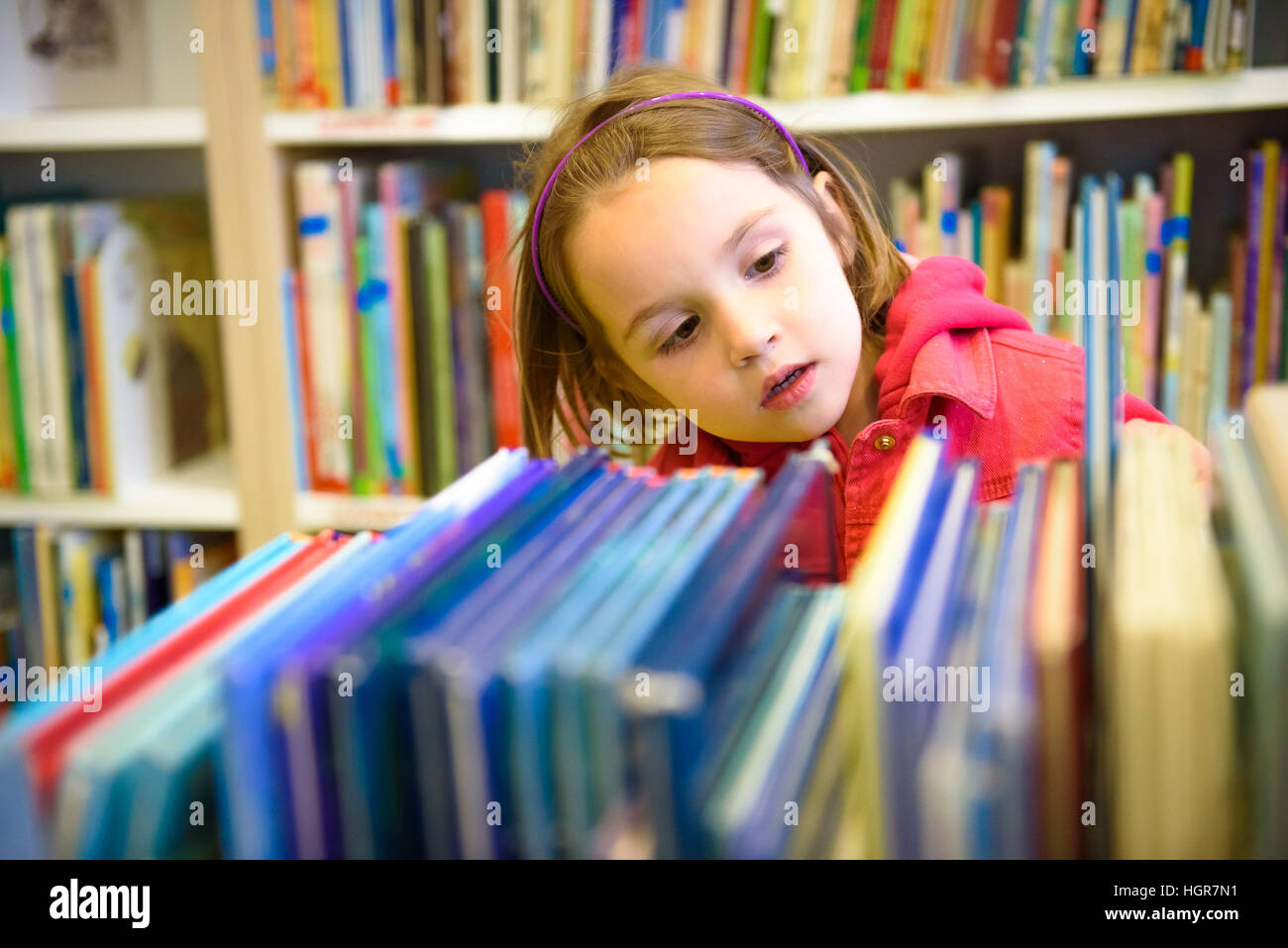 Little girl is choosing a book in the library. A child is looking at the books in the library deciding which one to take home. Children creativity and Stock Photo