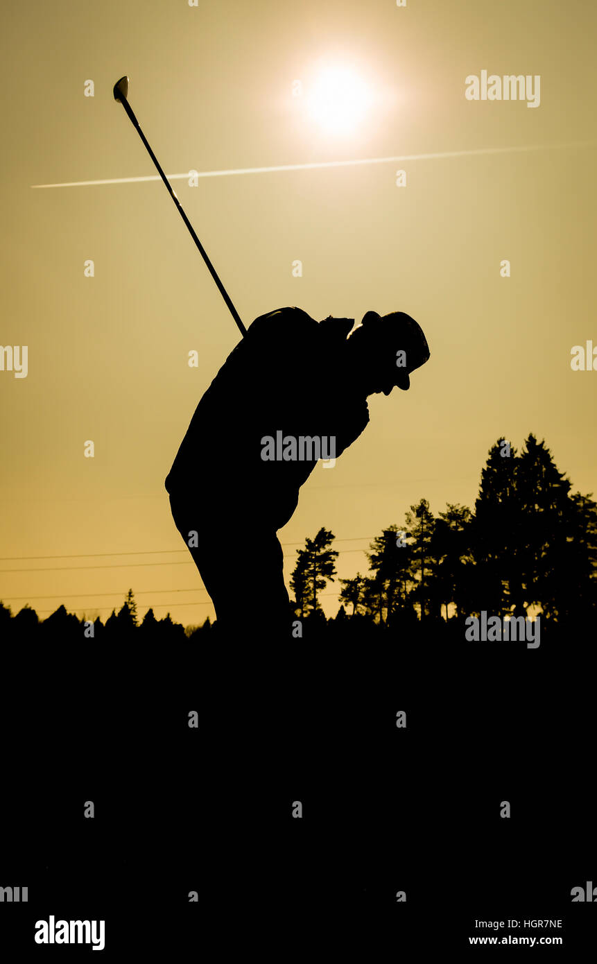 Silhouette of old man playing golf. Senior citizen is wearing a hat and swinging the club with sun and airplane contrails in the background. Also a si Stock Photo