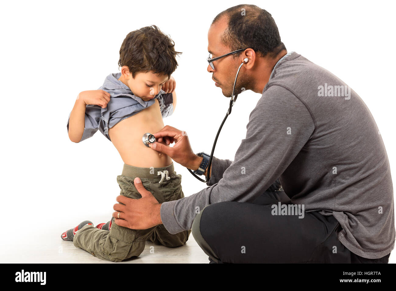 Doctor is checking a boy stomach with a stethoscope. Father and son are playing medical examination at the doctors office. Stock Photo