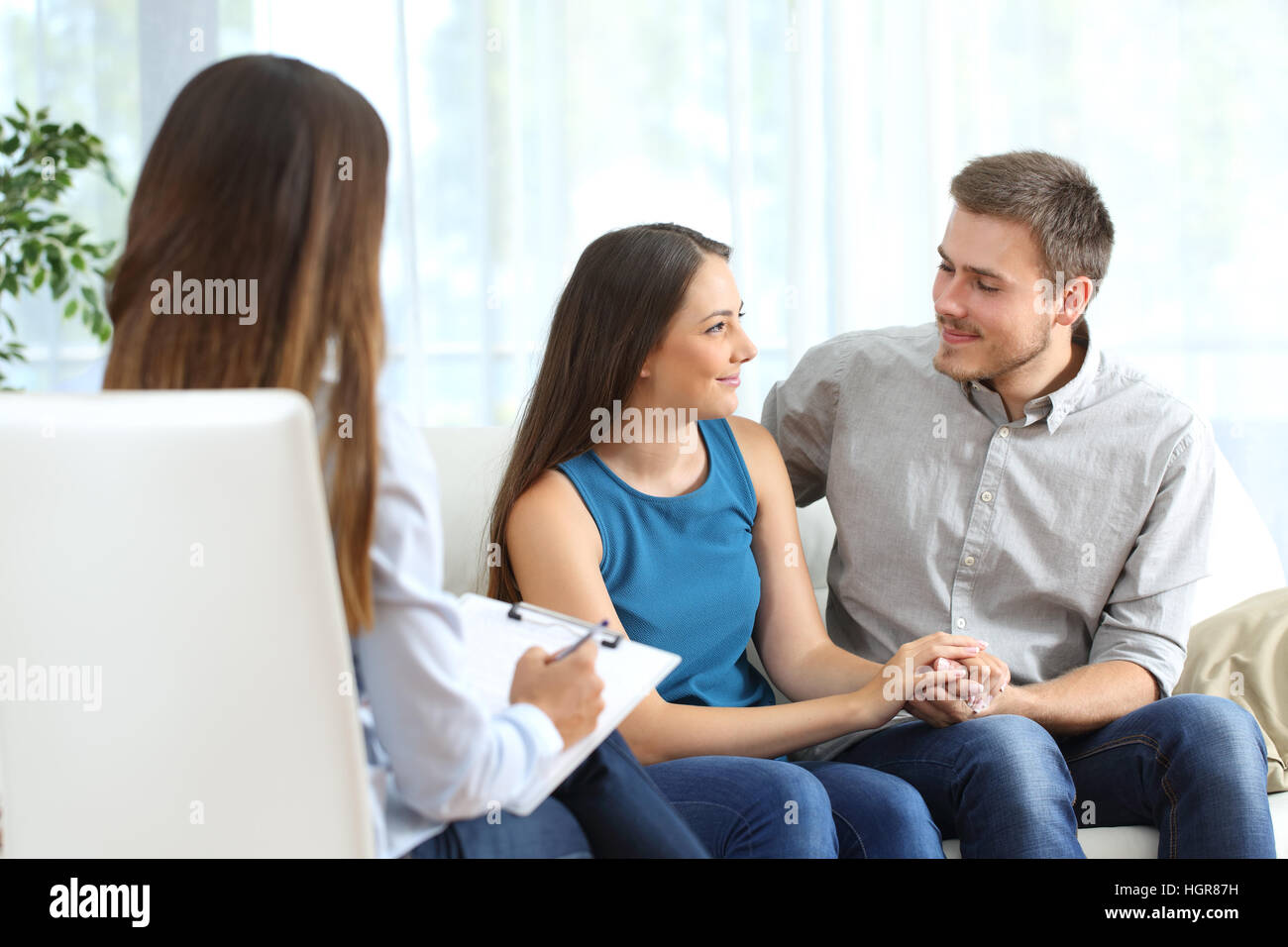 Happy couple listening to a marriage counselor and looking each other during therapy at home Stock Photo