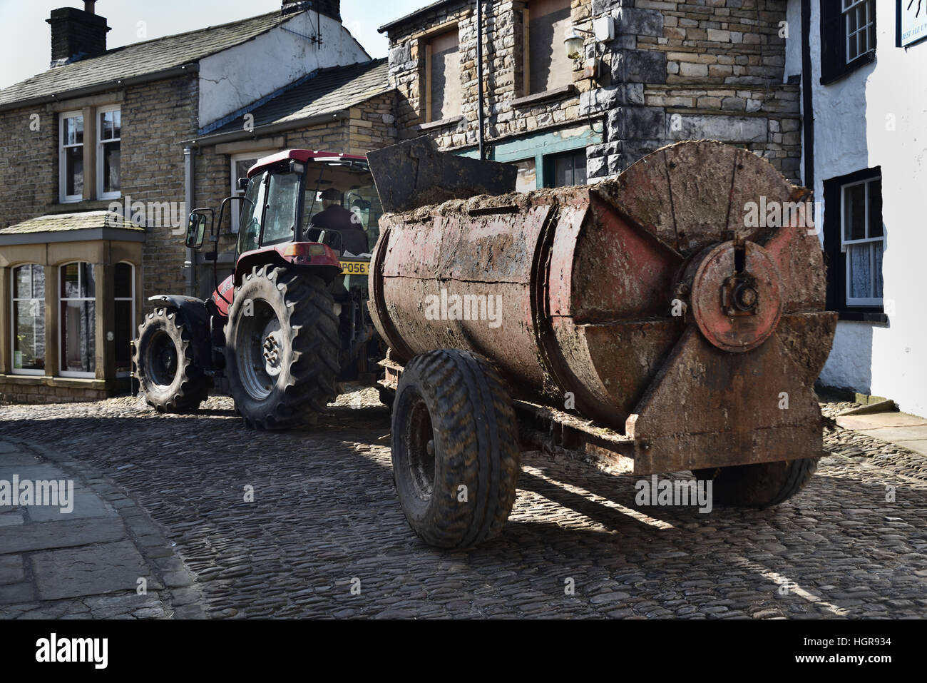 Tractor towing muck spreader, Main Street, Dent, Yorkshire Dales National Park, Cumbria, England, UK. Stock Photo