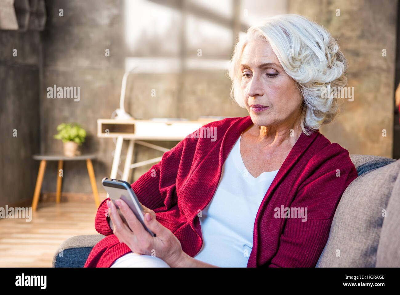 Portrait of senior woman using smartphone while sitting on sofa Stock Photo