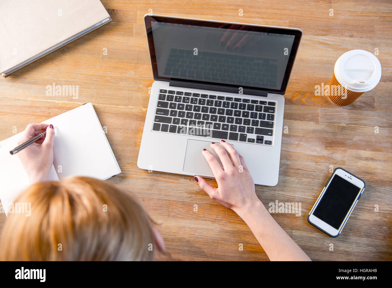 Top view of young woman using laptop and making notes in notebook Stock Photo