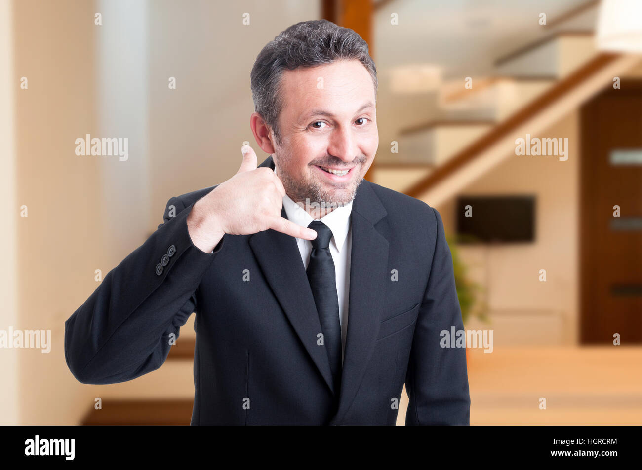 Cheerful real estate agent doing a call gesture with hand and smiling ...