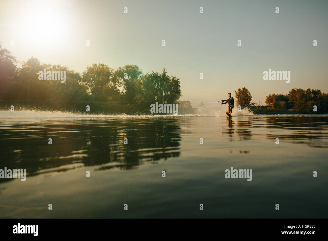 Outdoor shot of man wakeboarding on lake at sunset. Water skiing on lake behind a boat. Stock Photo