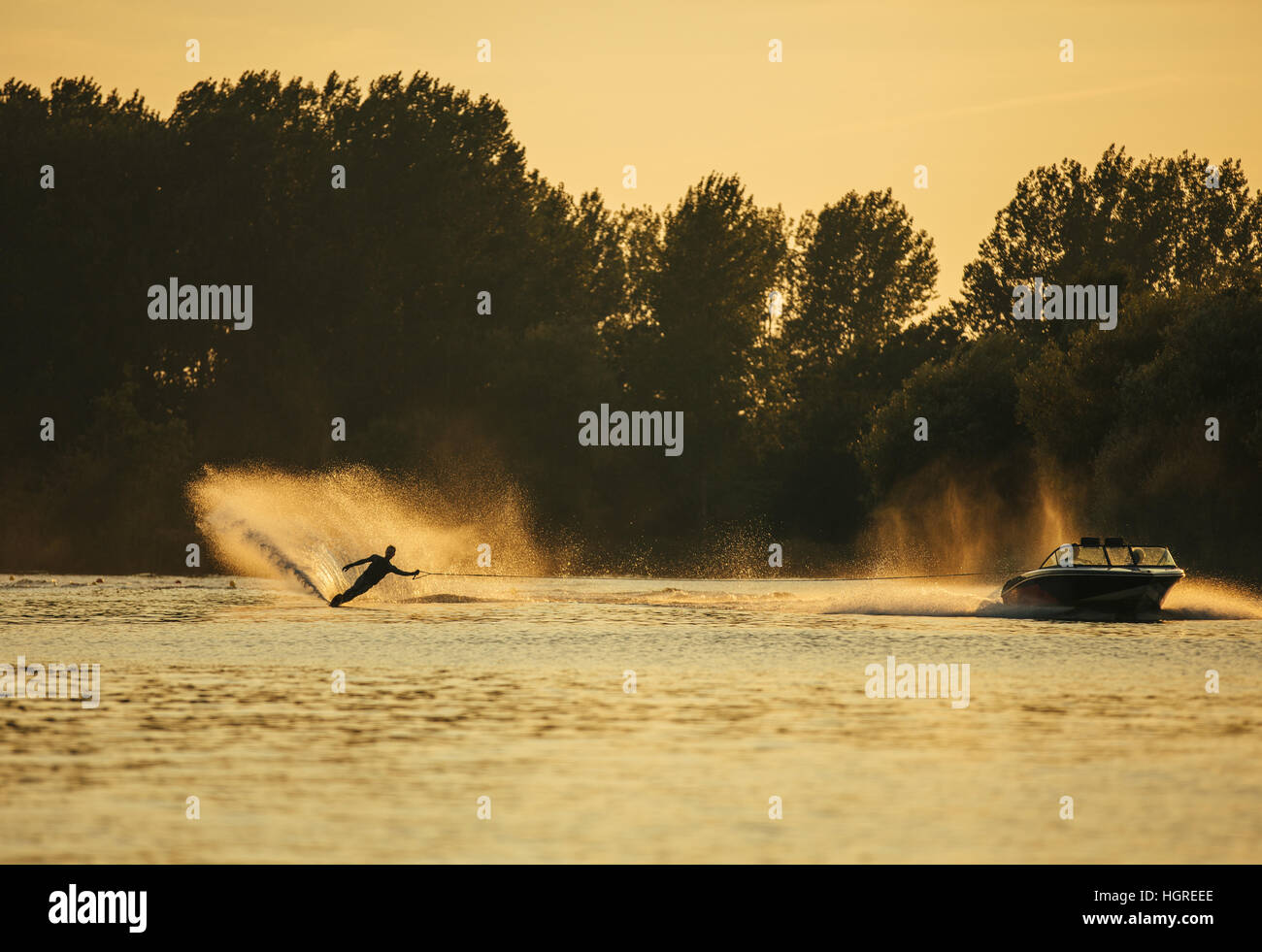 Man wakeboarding on lake behind boat at sunset. Water skiing on lake. Stock Photo