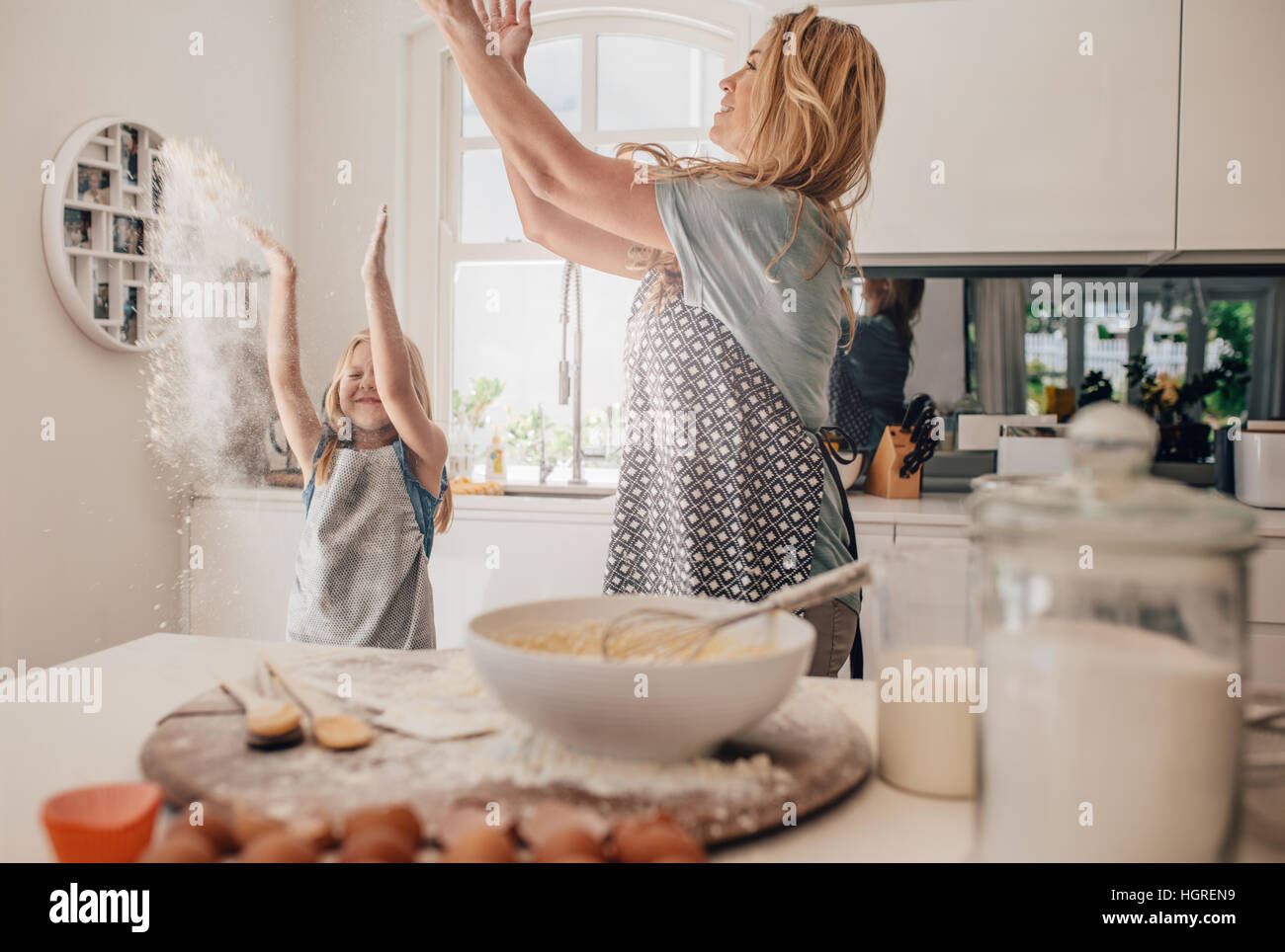 Happy young family having fun in kitchen throwing flour in air. Mother and daughter making dough in kitchen. Stock Photo