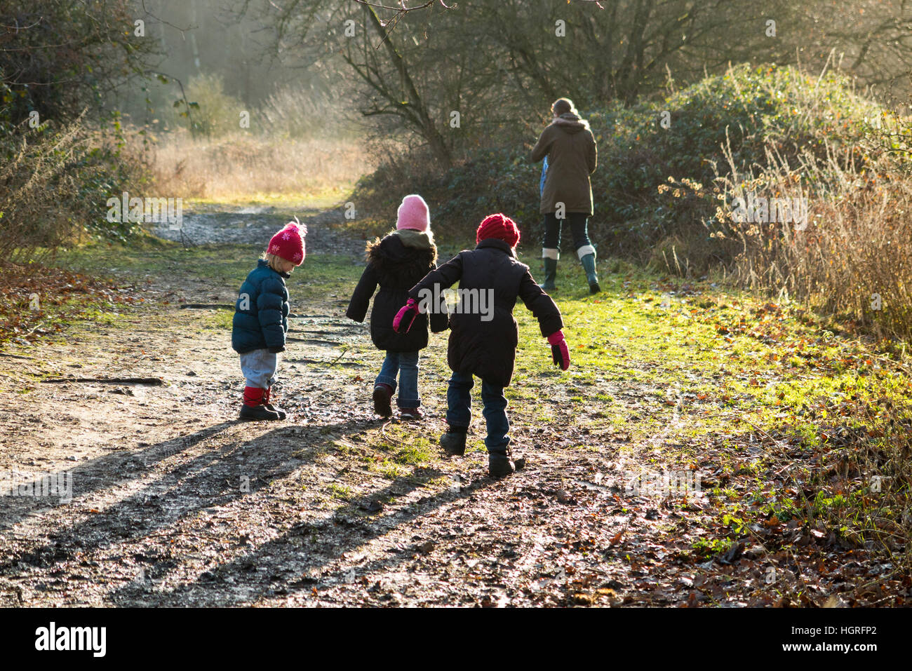 Mother & 3 children three kids daughters walking / walk along muddy path / in mud on walkway pathway foot path footpath Esher UK Stock Photo