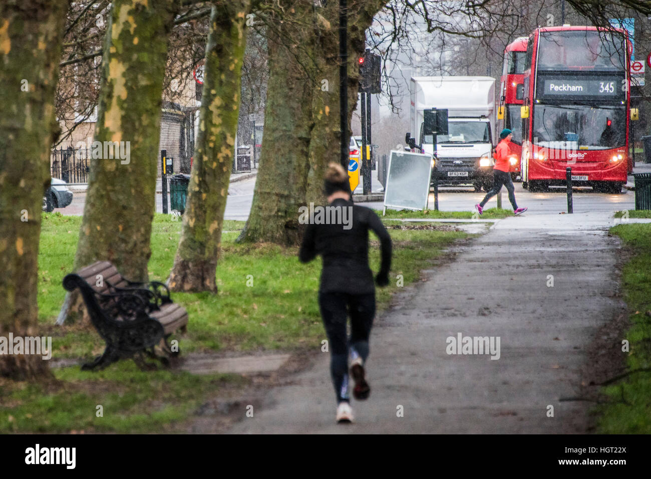 London, UK. 13th Jan, 2017.   Vehicle lights are onin the gloom approaching the Northside - A blizzard of snow sweeps across Clapham Common with an icy Northerly wind. Even so it does not deter dog walkers, joggers and cyclists. © Guy Bell/Alamy Live News  Stock Photo