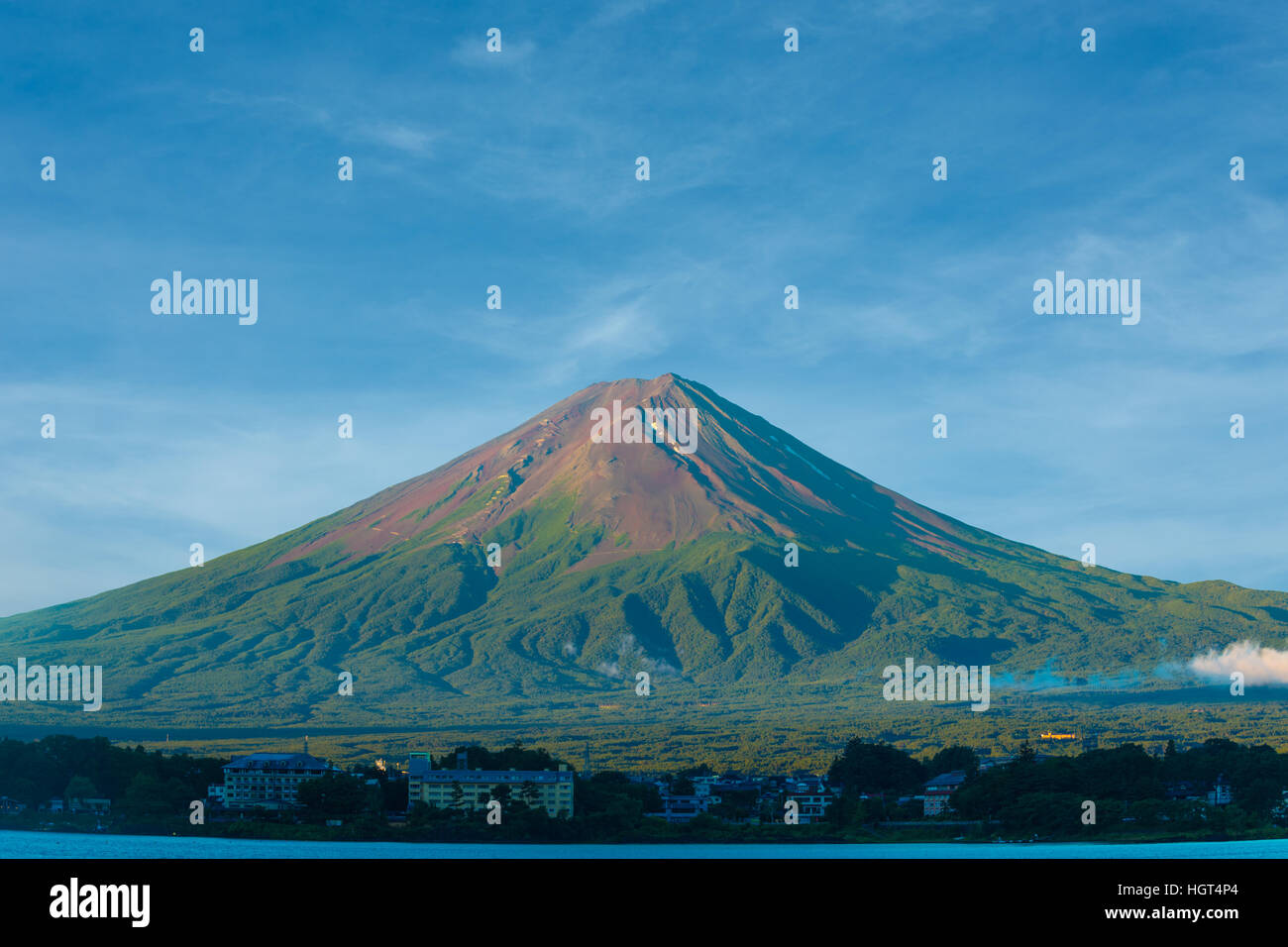 No snow on dirt volcanic cone of Mount Fuji with foreground hotels of Lake Kawaguchiko during summer morning below a lovely blue Stock Photo