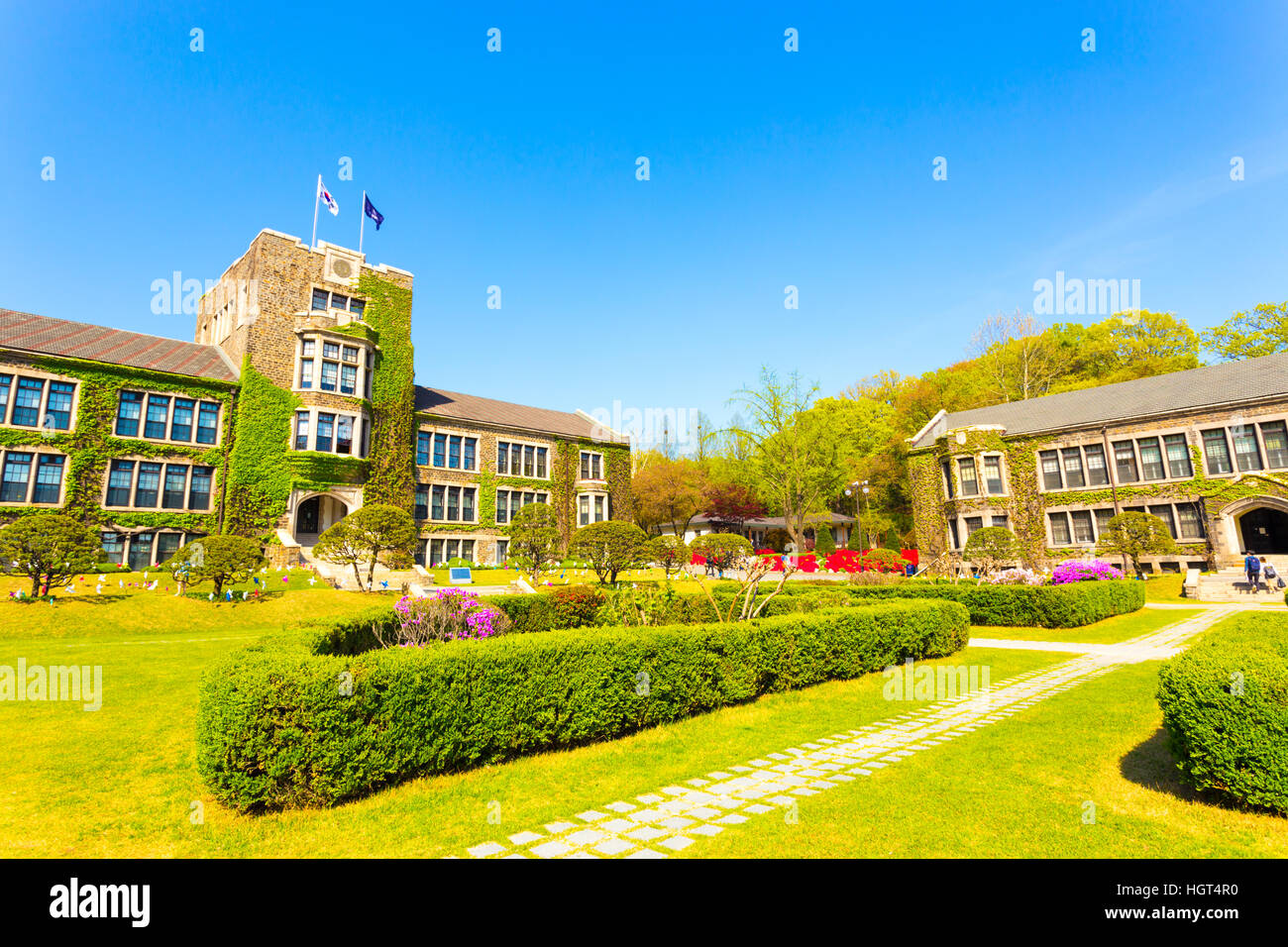 Wide angle view of flags flying over ivy covered main building above grassy quad at Yonsei University in Sinchon, Seoul Stock Photo