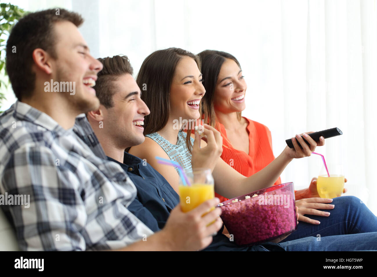 Side view of a happy group of four friends watching and enjoying tv sitting on a sofa in the living room at home Stock Photo