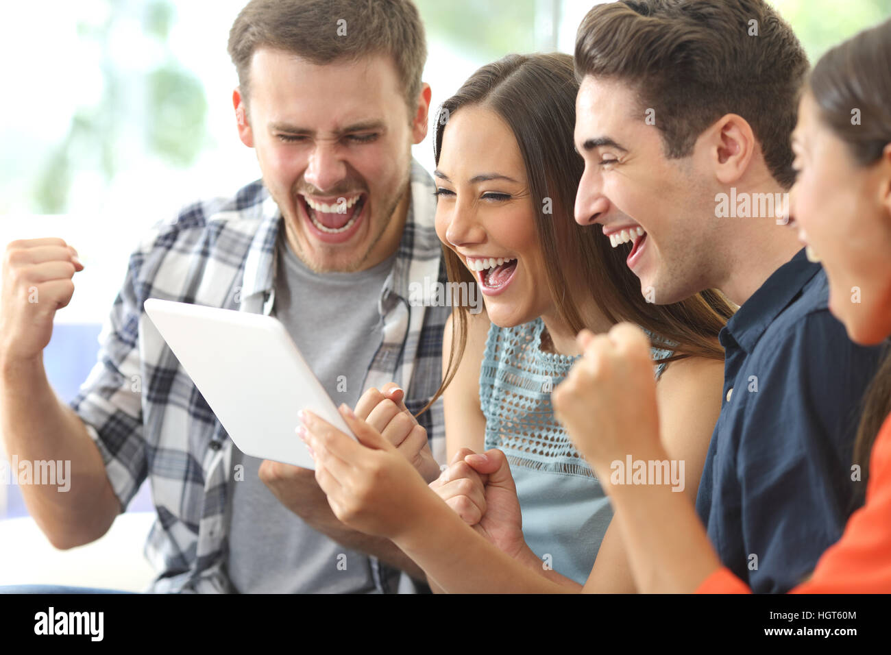 Excited group of four friends viewing media content on line from a tablet in a house interior Stock Photo