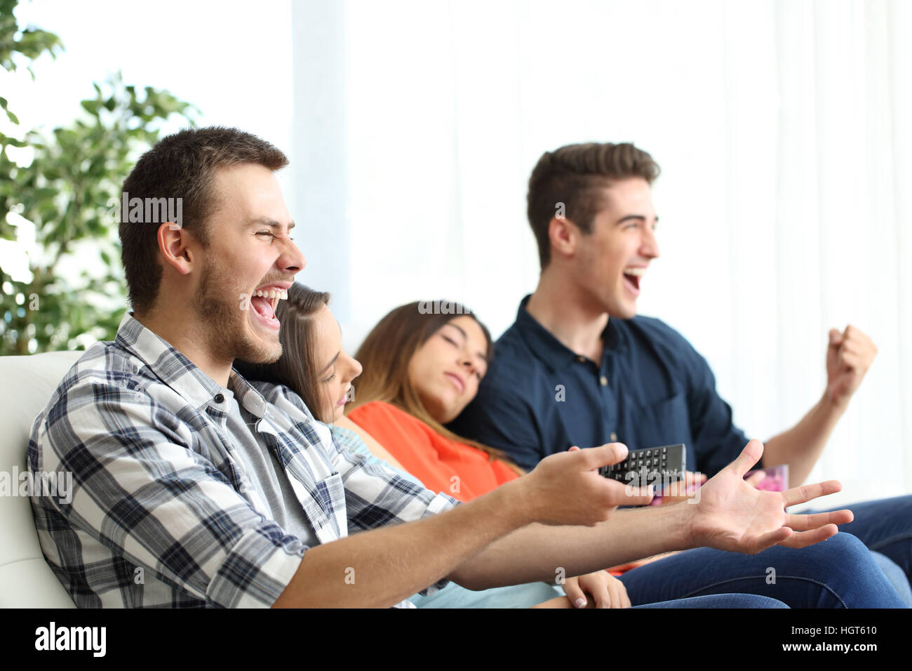 Excited men watching tv and bored girlfriends sitting on a couch in the living room at home Stock Photo