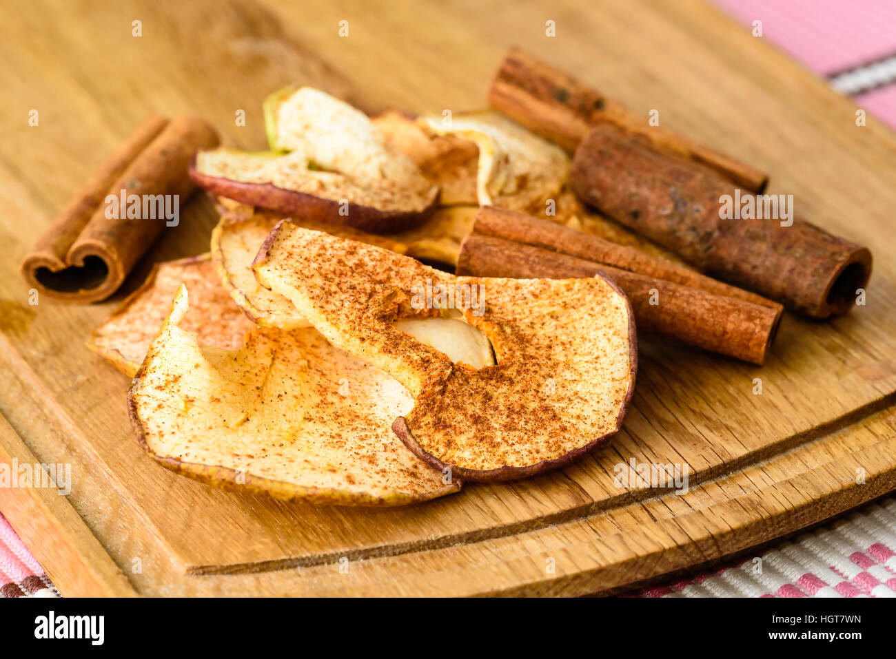 Dehydrated apple slices with powdered cinnamon and whole cinnamon on wooden cutting board. Stock Photo
